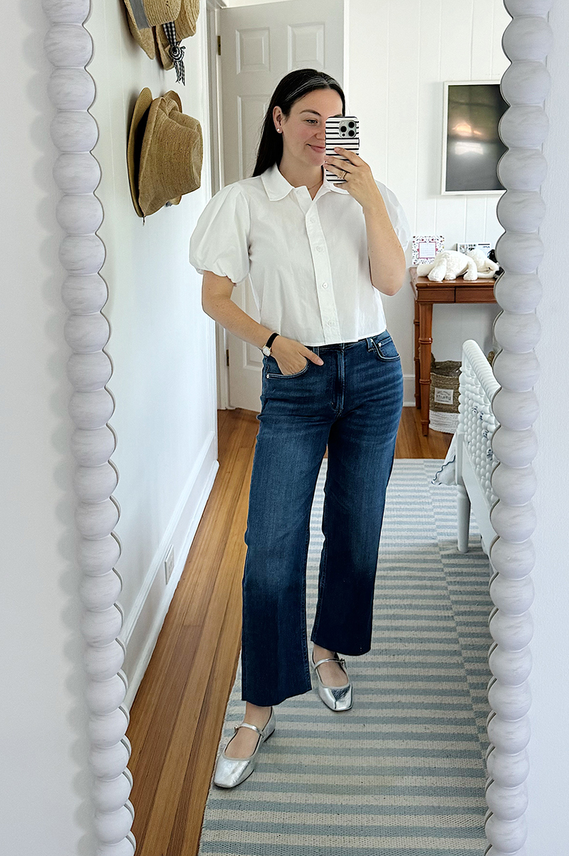 A mirror selfie of Carly wearing dark denim jeans and a white puff sleeve blouse.