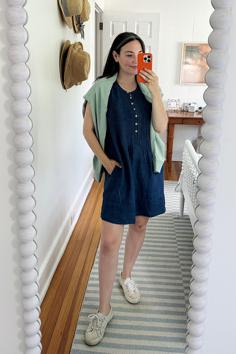 A mirror selfie of Carly wearing a denim dress and a green sweatshirt over her shoulder. 