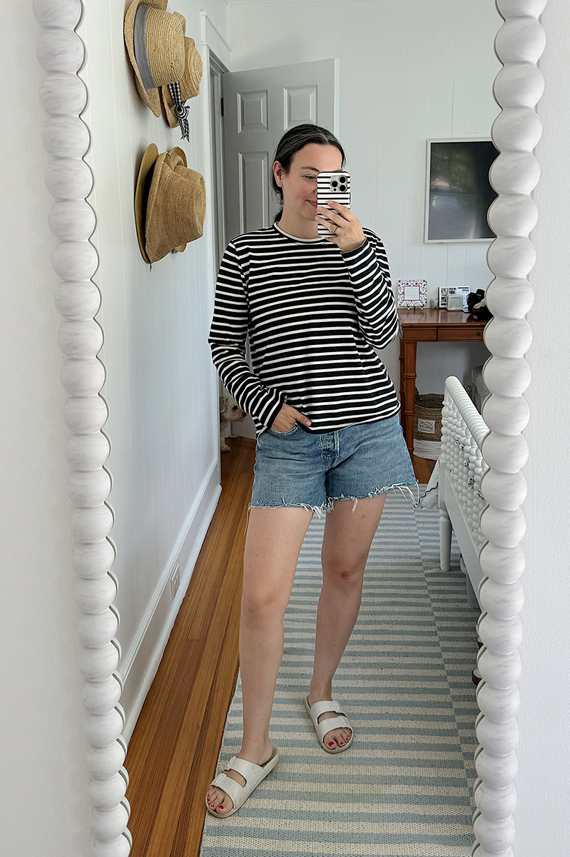 A mirror selfie of Carly wearing denim cut off shorts and a navy and white striped shirt.