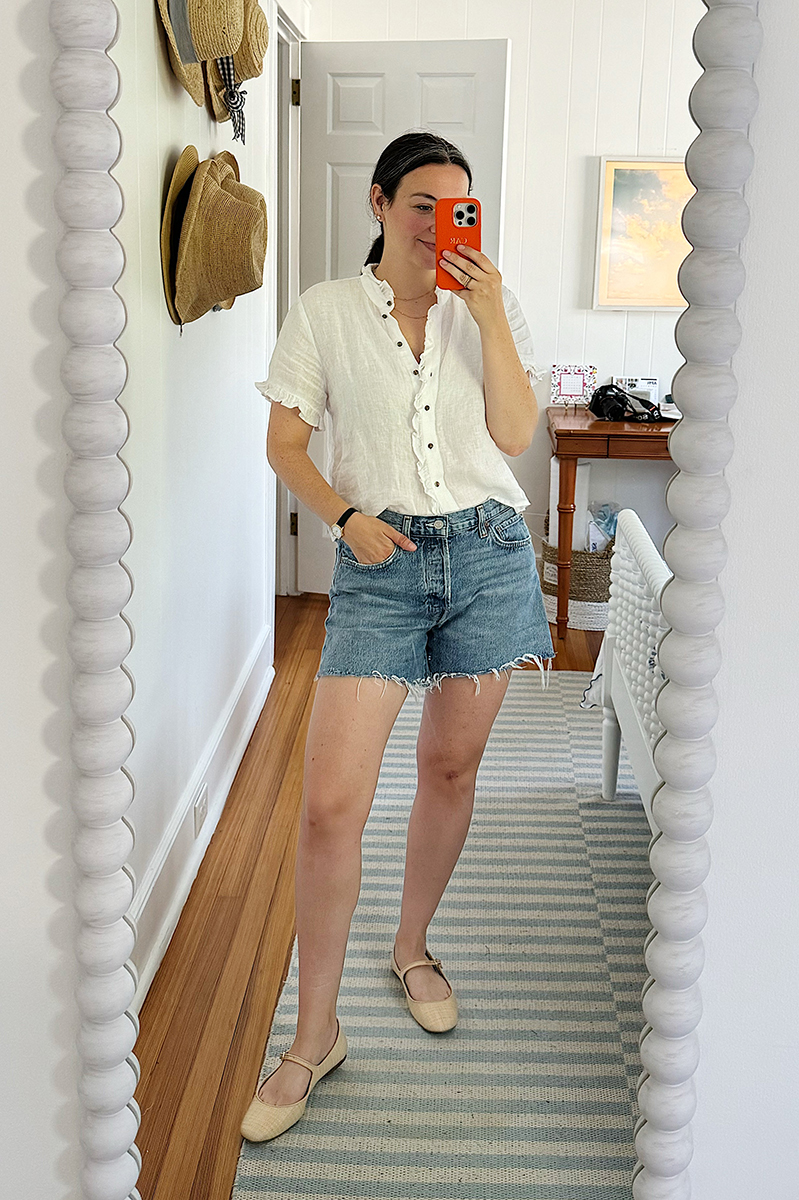 A mirror selfie of Carly wearing blue denim shorts and a white ruffle linen shirt from J. Crew. 