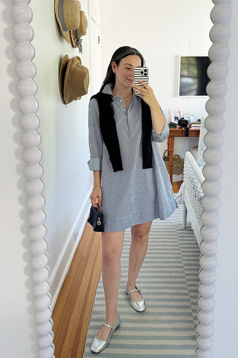 A mirror selfie of Carly wearing a blue and white striped swing dress with a sweater over her shoulders and metallic mary janes.