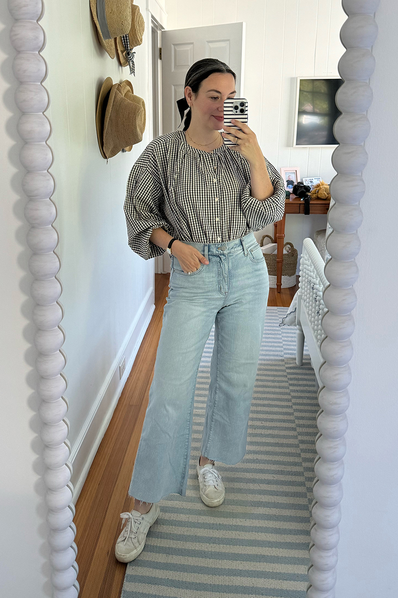 A mirror selfie of Carly wearing a black and white gingham top and wide legged light wash jeans. 