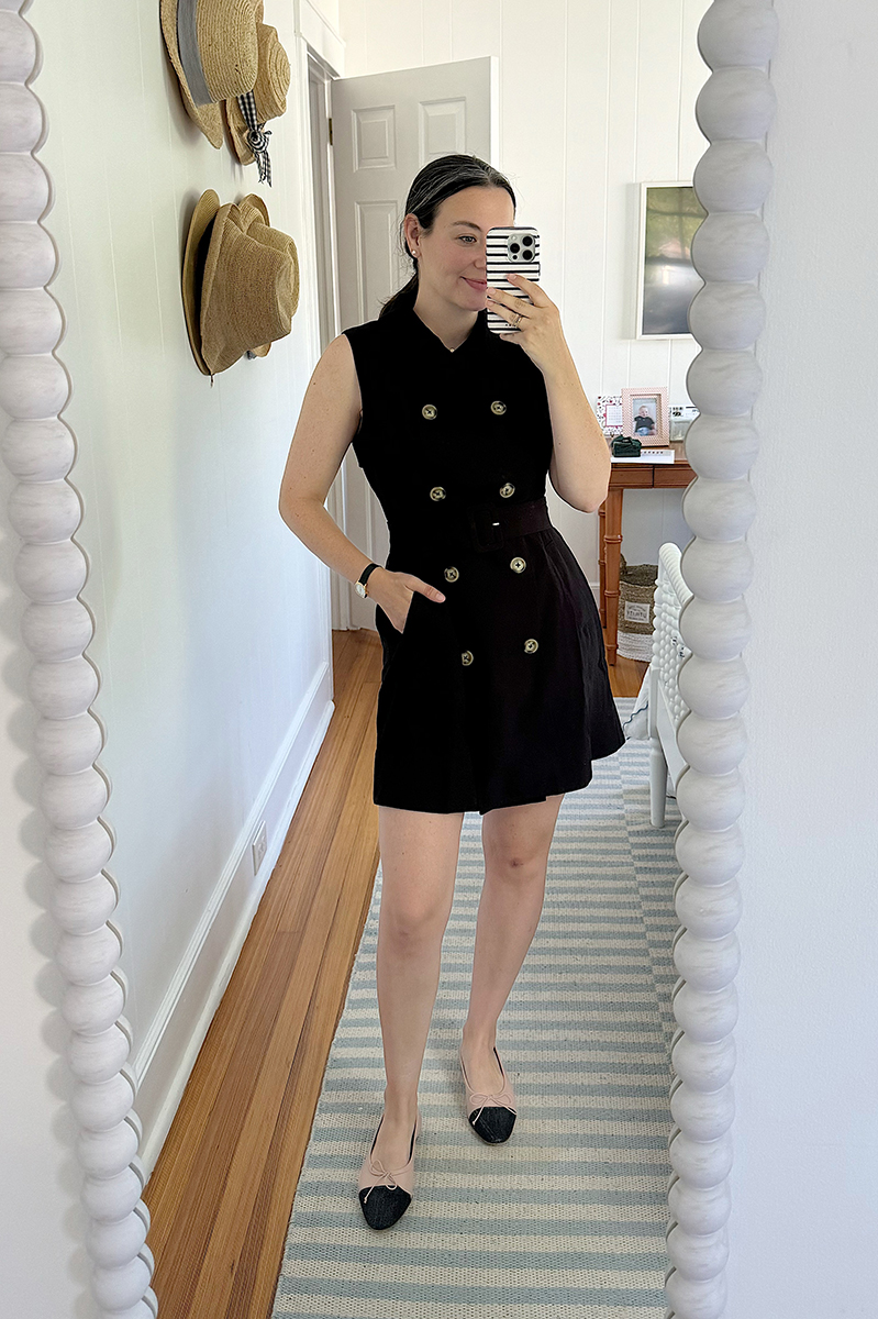 A mirror selfie of Carly wearing a black double breasted dress with cap toe ballet flats.