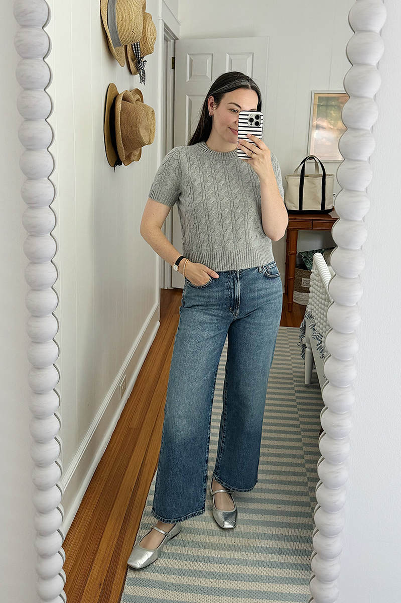 Carly taking a mirror selfie wearing a grey sweater and blue jeans.