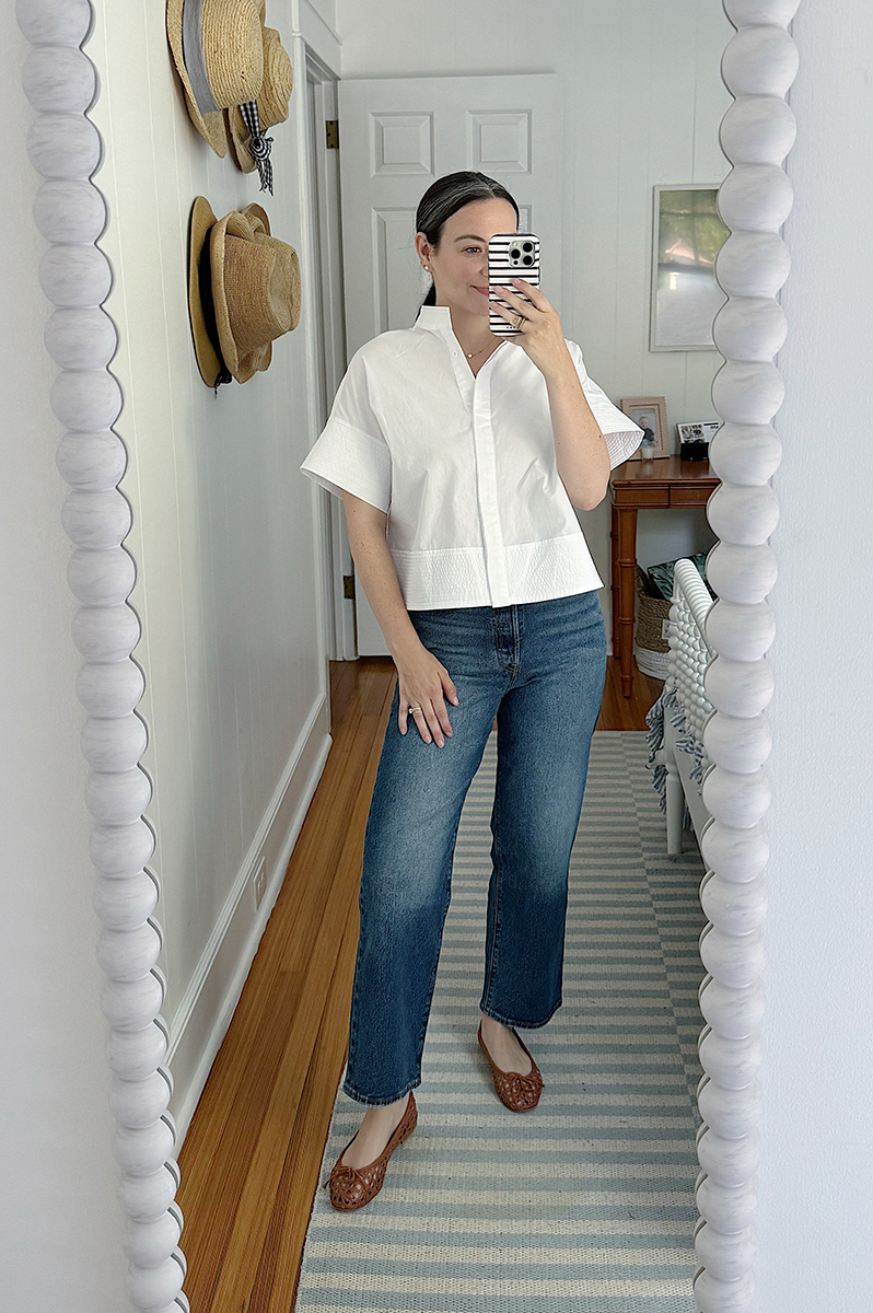 Carly taking a mirror selfie wearing a white blouse and blue jeans.