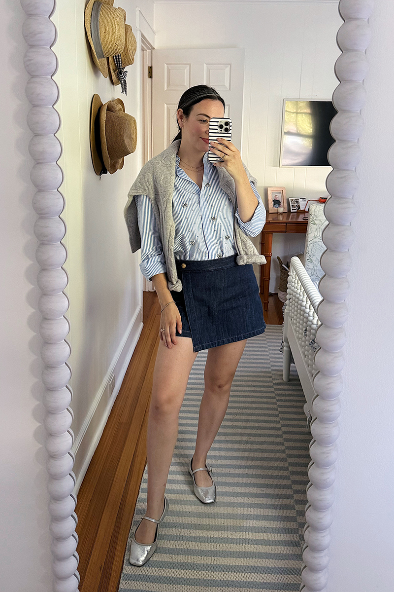 Carly taking a mirror selfie wearing a blue button up and denim skort.