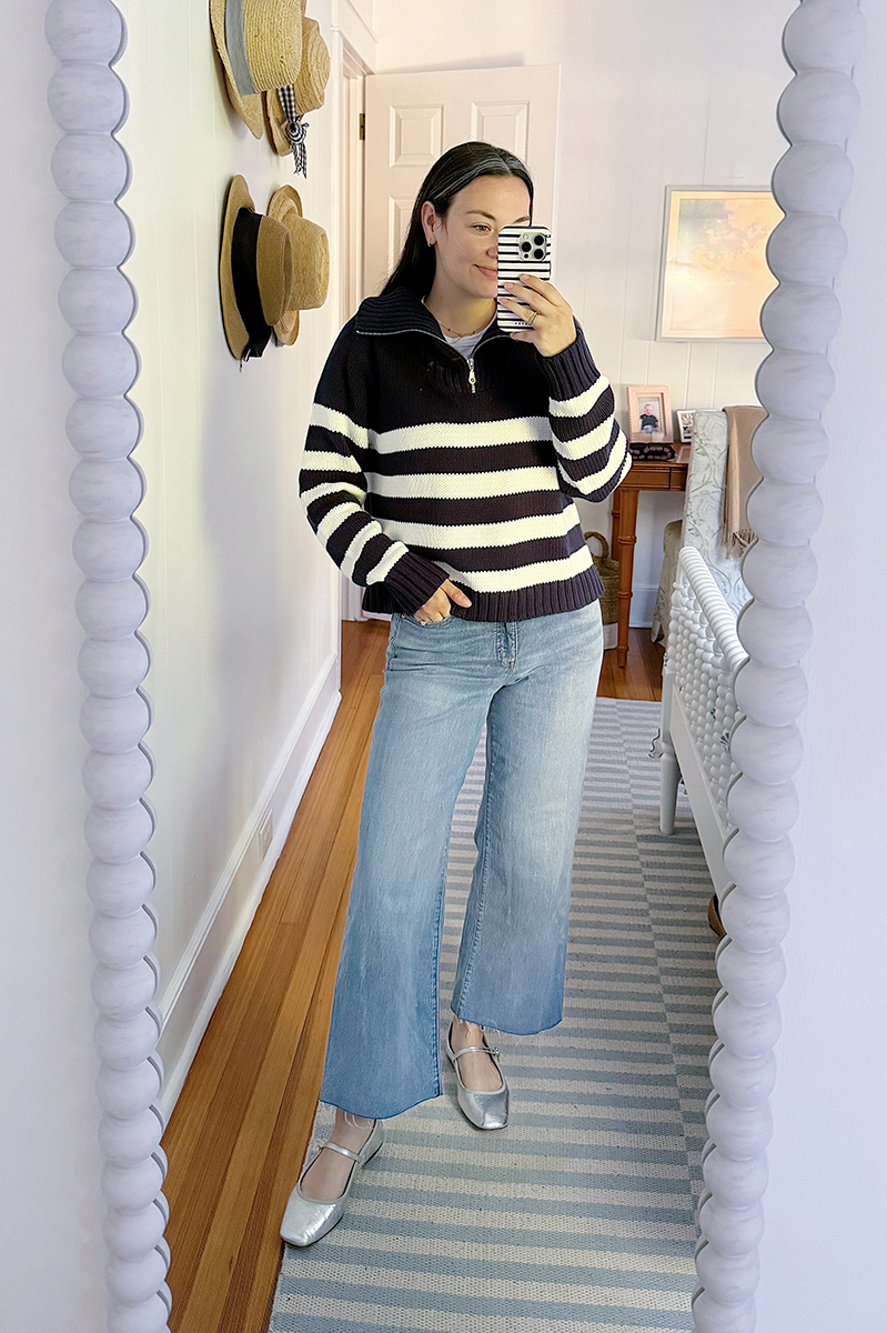 Carly taking a mirror selfie wearing wide legged jeans, metallic mary janes, and a striped sweater.