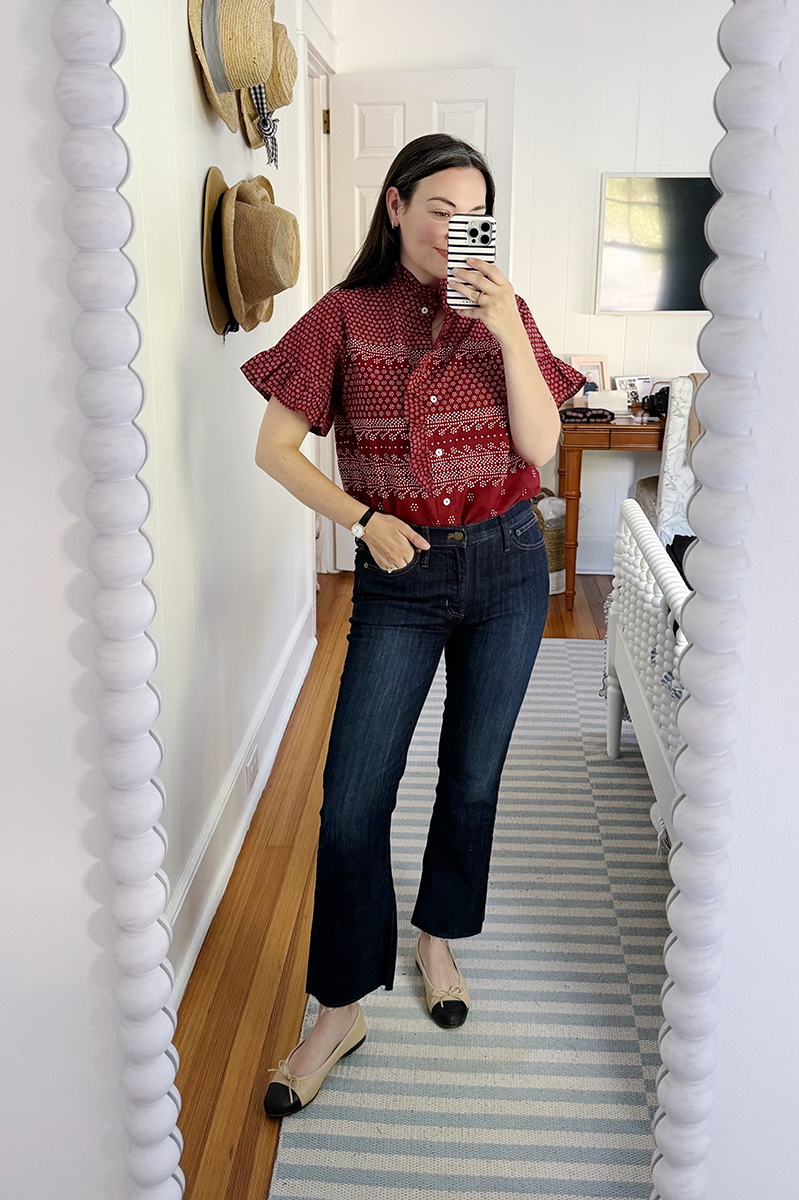 Carly taking a mirror selfie wearing a red blouse and dark denim jeans.