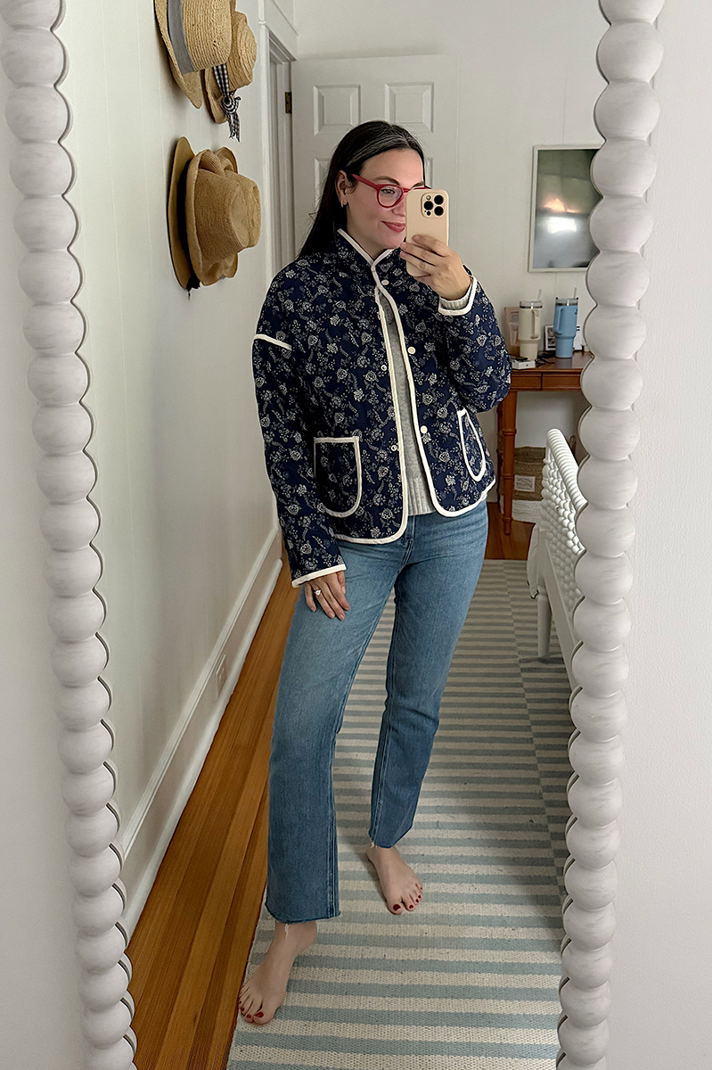 Carly Riordan taking a mirror selfie wearing a quilted jacket and jeans.