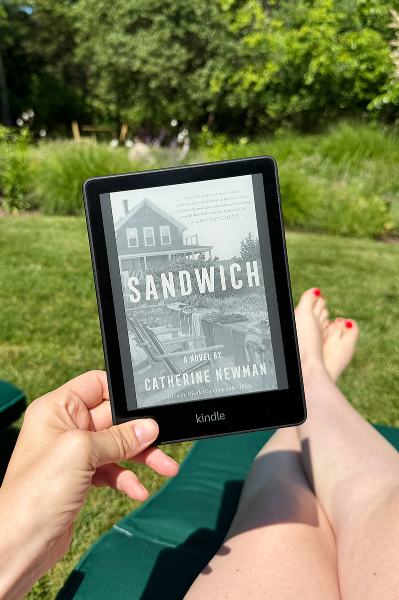 Carly holding her kindle with Sandwich book by Catherine Newman