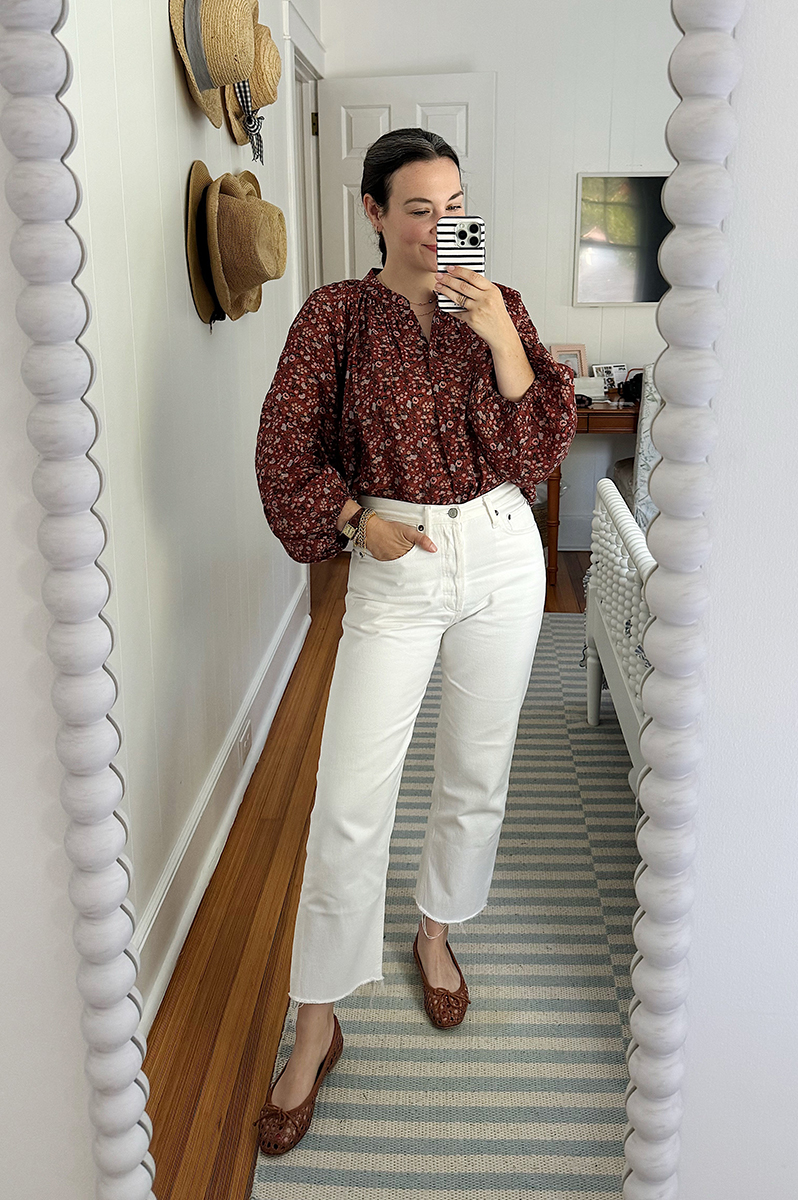 Carly taking a mirror selfie wearing white jeans and a burgundy floral blouse.