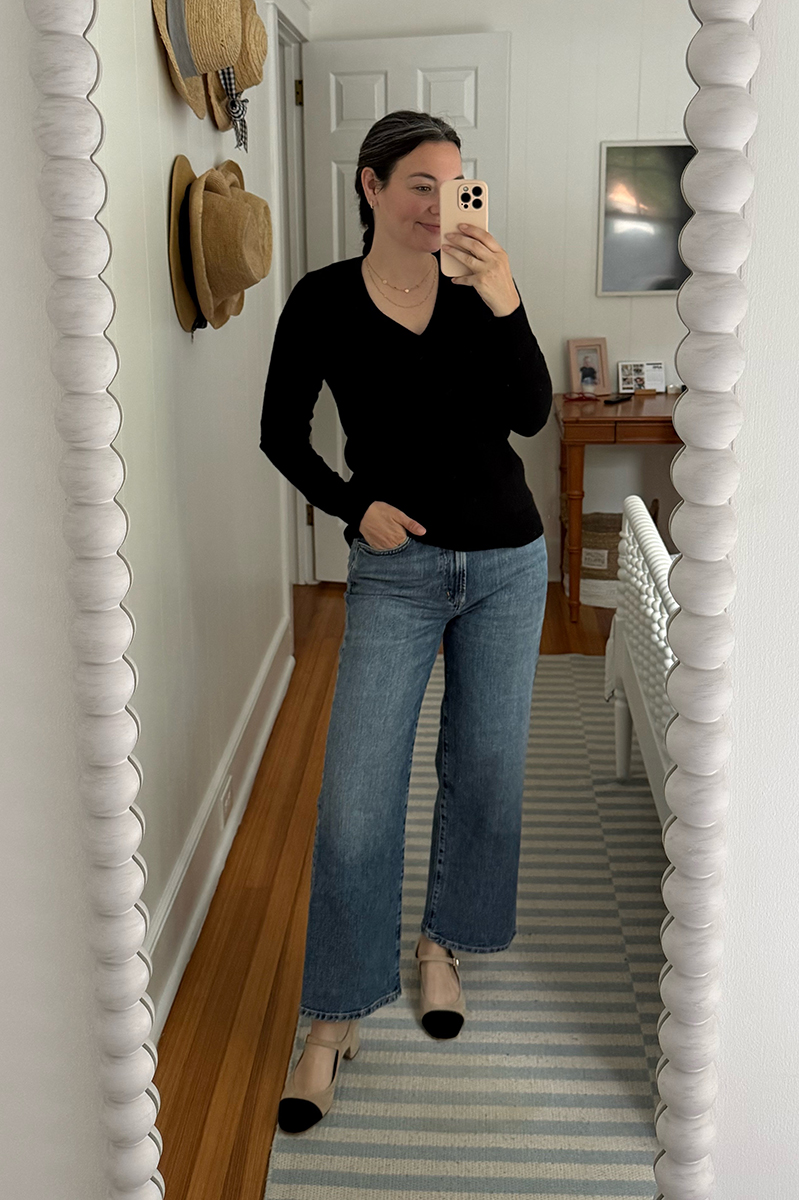 Carly Riordan taking a mirror selfie wearing a v-neck sweater and wide legged jeans.