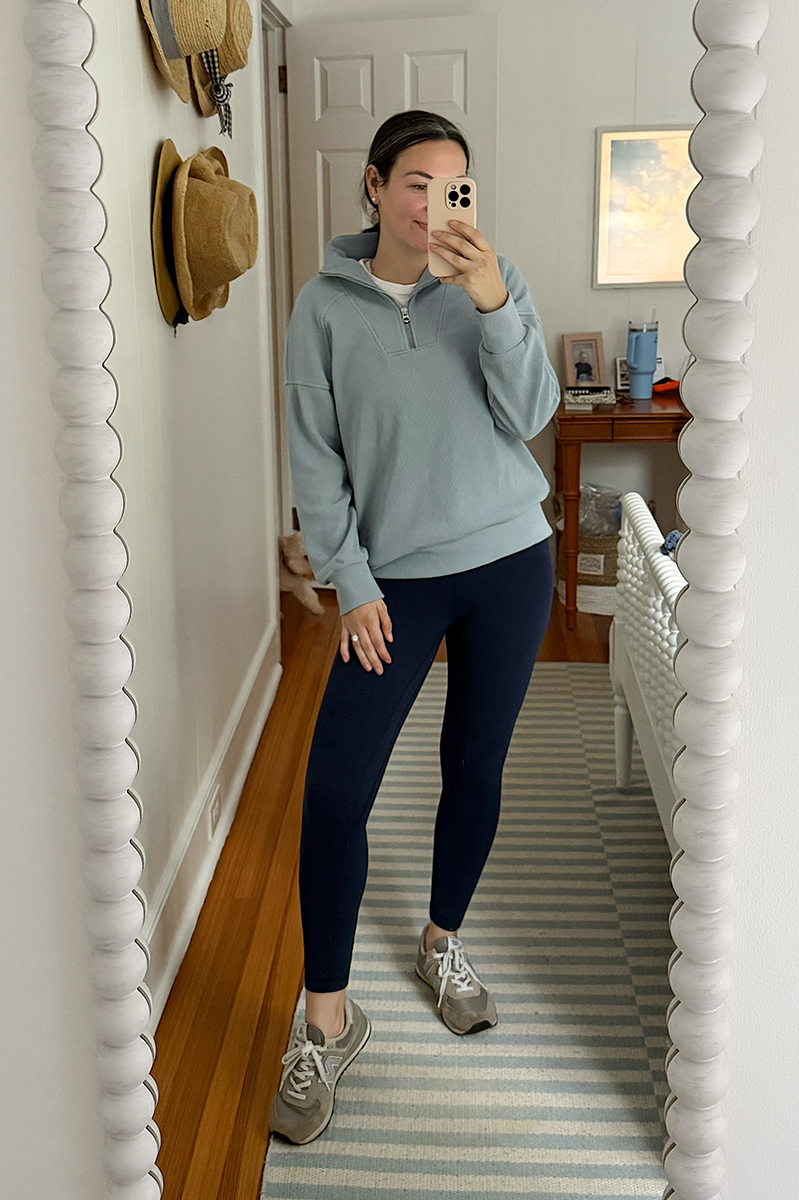 Carly Riordan taking a mirror selfie wearing a blue pullover and navy leggings.