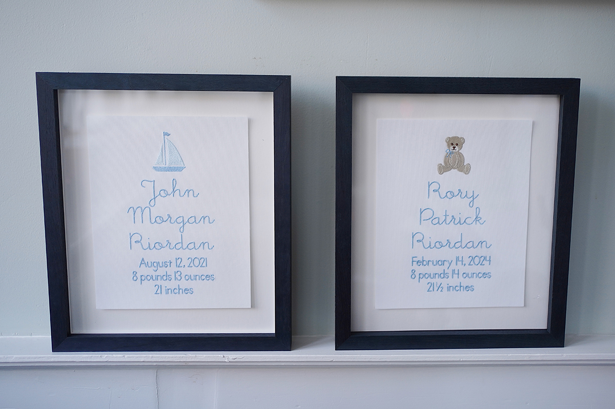 Two embroidered birth announcements in navy frames