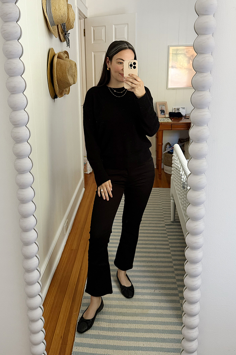 Carly Riordan in a mirror selfie wearing a black sweater and boot cropped jeans and ballet flats. 