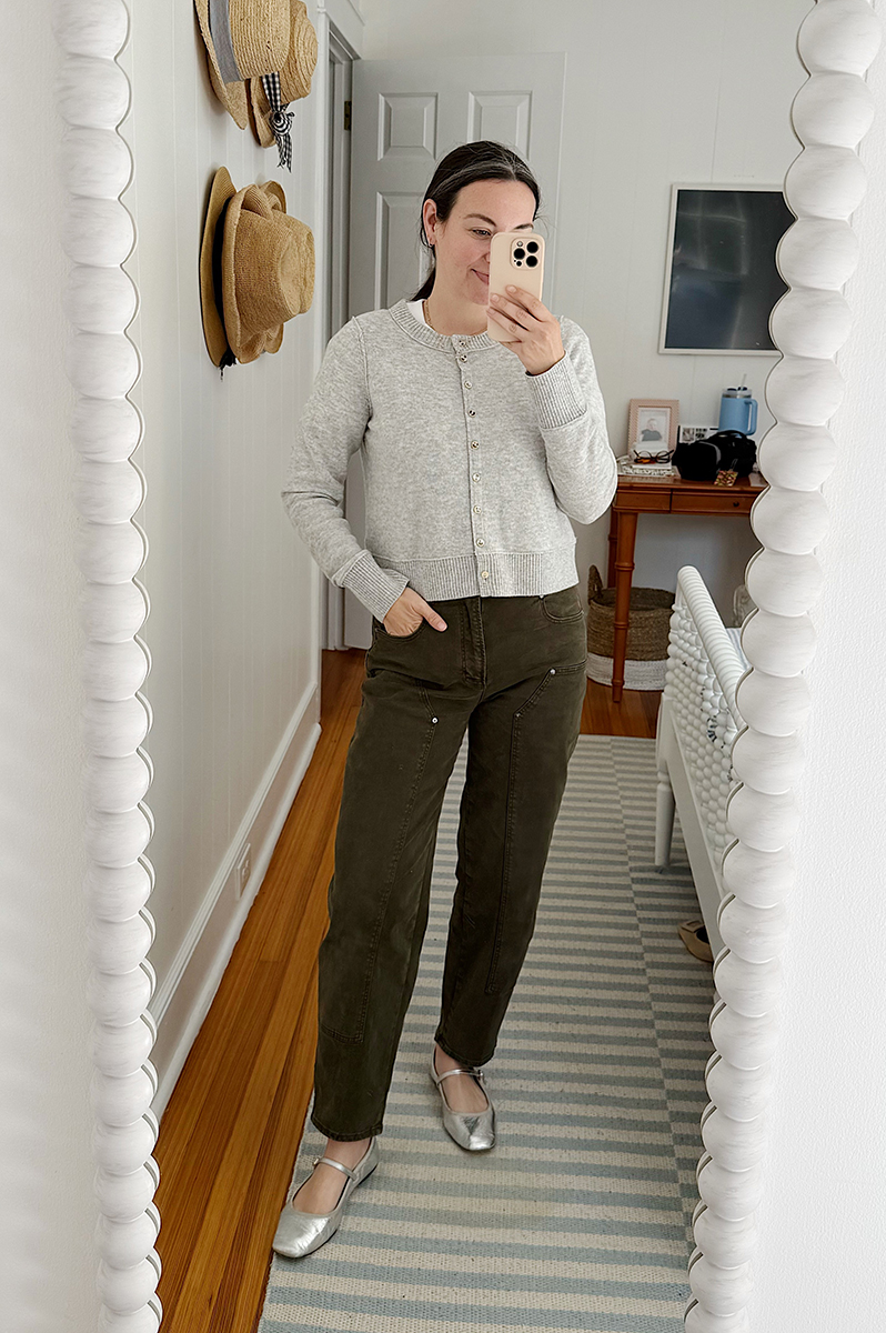 Carly Riordan in a mirror selfie wearing green pants and a grey cardigan.