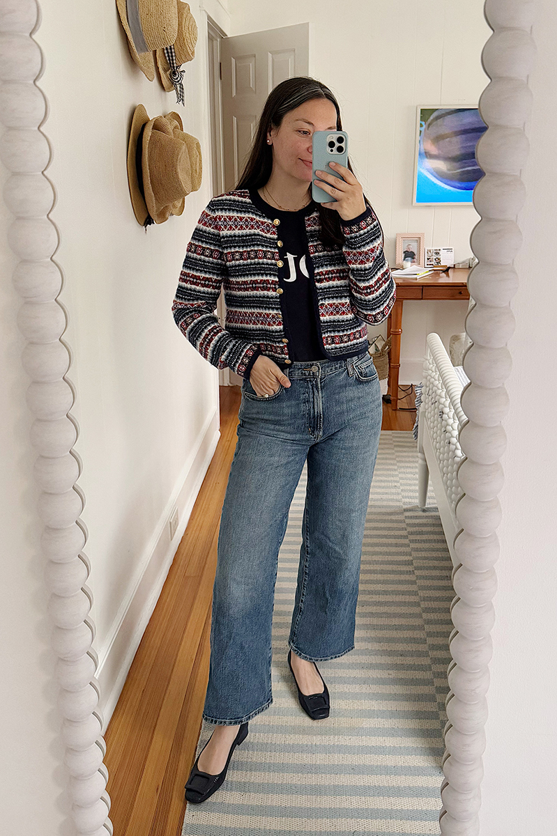 Carly Riordan taking a mirror selfie wearing a fair isle cardigan and wide legged jeans.