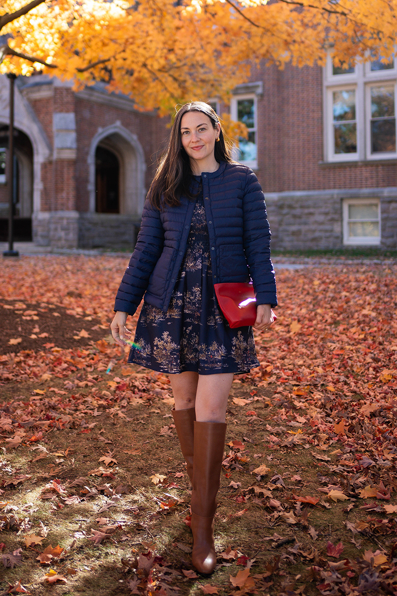 Carly Riordan wearing a Vivi nap dress with a fall toile print and tall boots and a navy puffer vest.