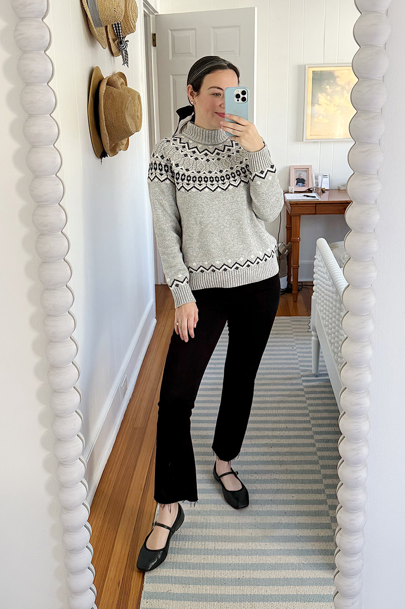 Carly Riordan taking a mirror selfie wearing a fair isle sweater and black pants. 