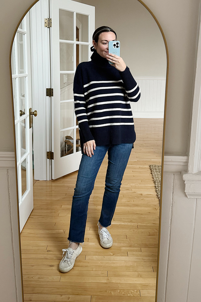 Carly Riordan taking a mirror selfie wearing a striped turtleneck and jeans.