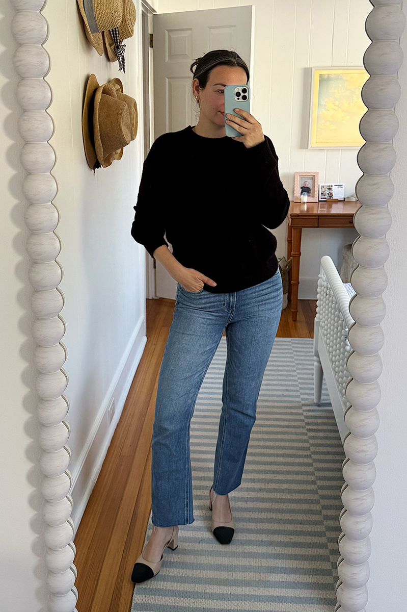 Carly Riordan taking a mirror selfie wearing a black cashmere sweater and cap toe block heels.