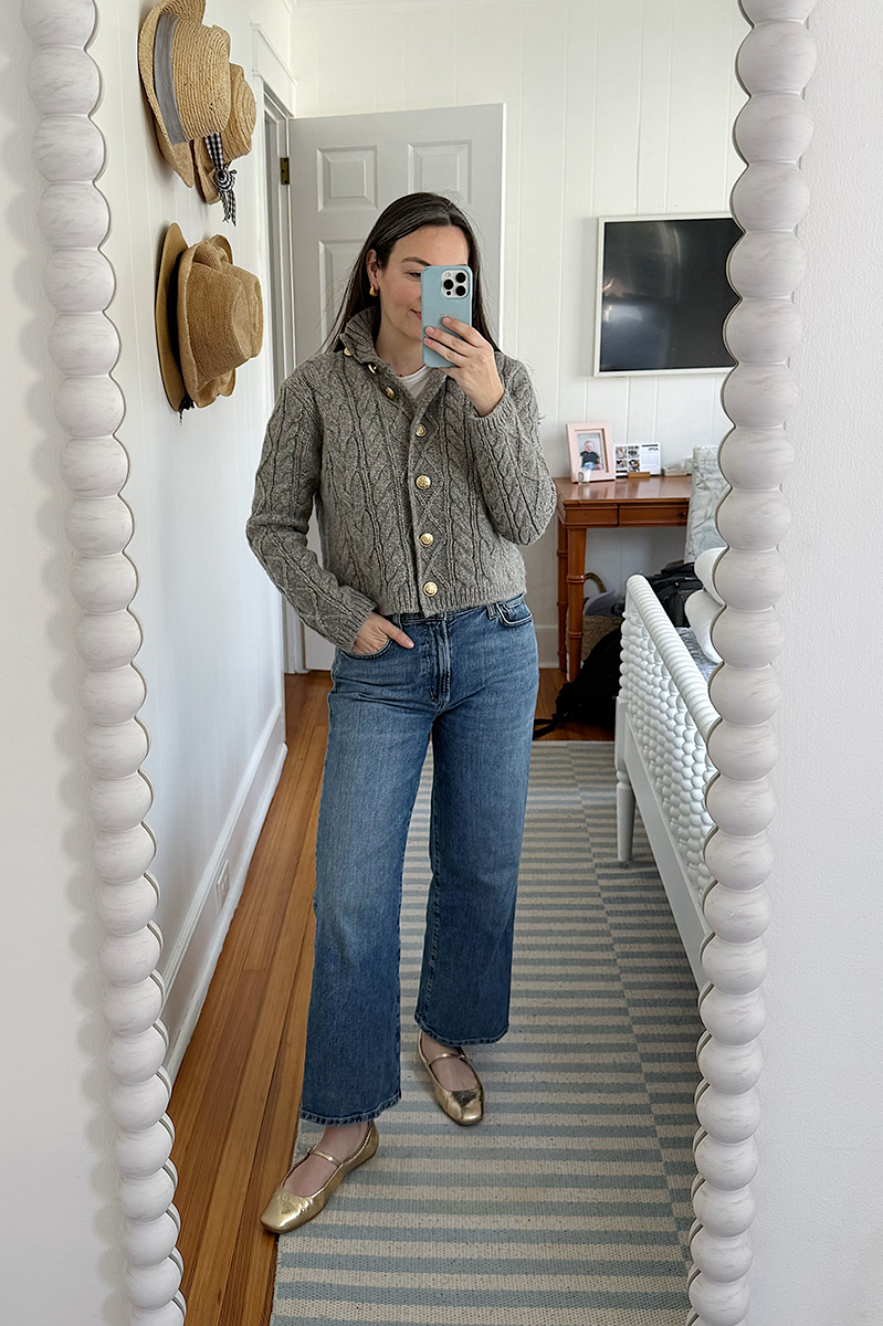 Carly Riordan taking a mirror selfie wearing a cashmere cable knit sweater, wide leg jeans, and mary janes.