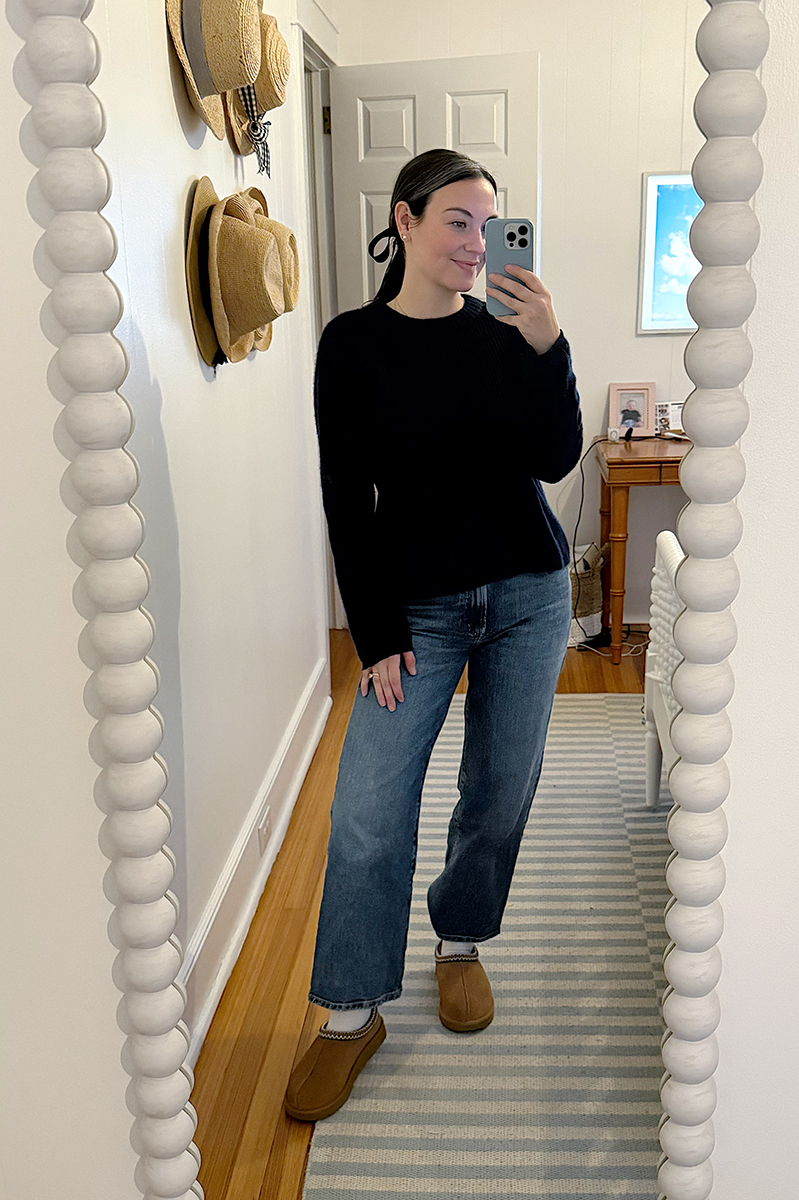 Carly Riordan taking a mirror selfie wearing a navy sweater and ugg slip ons.