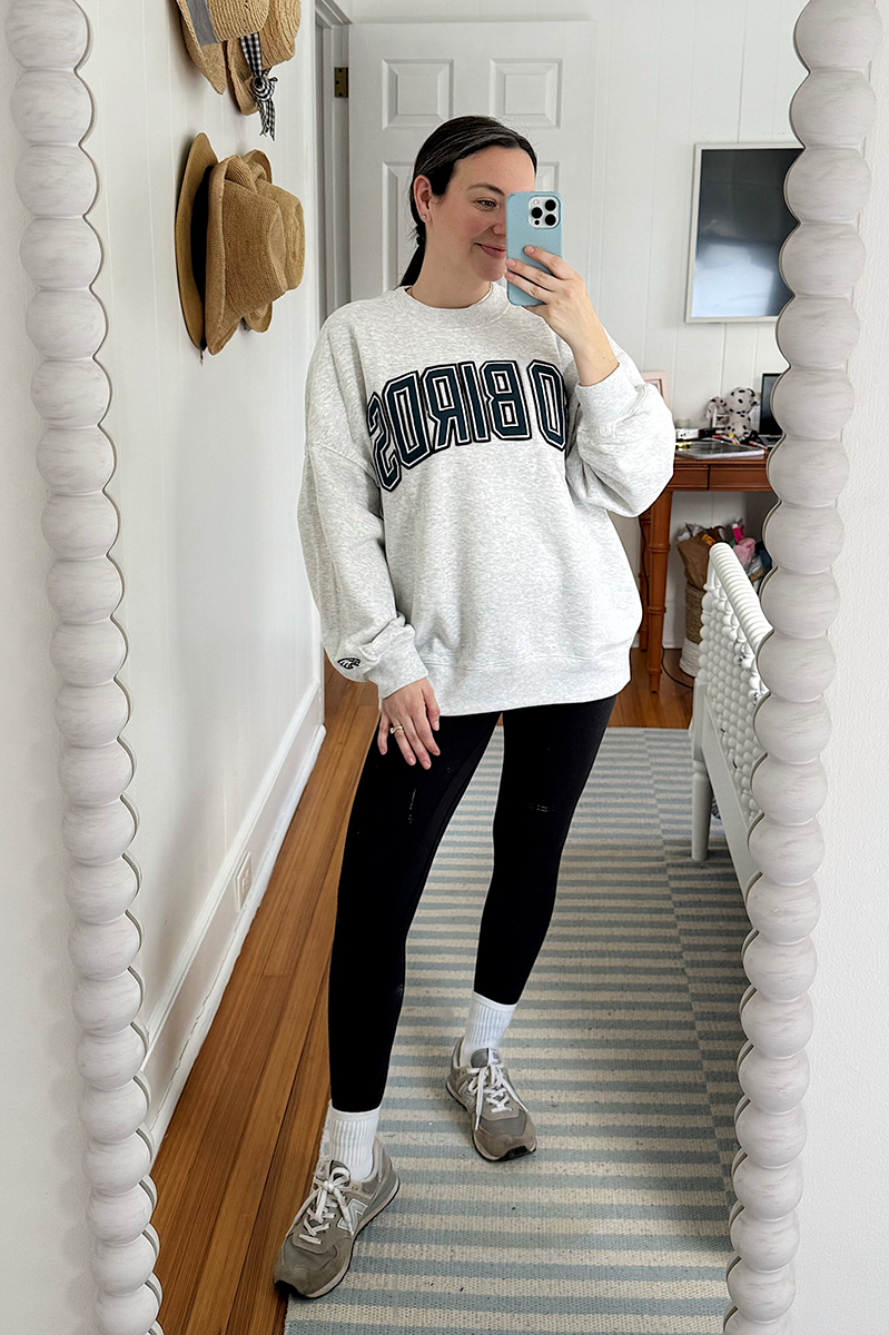 Carly Riordan taking a mirror selfie wearing an oversized Eagles sweatshirt, leggings, and sneakers.