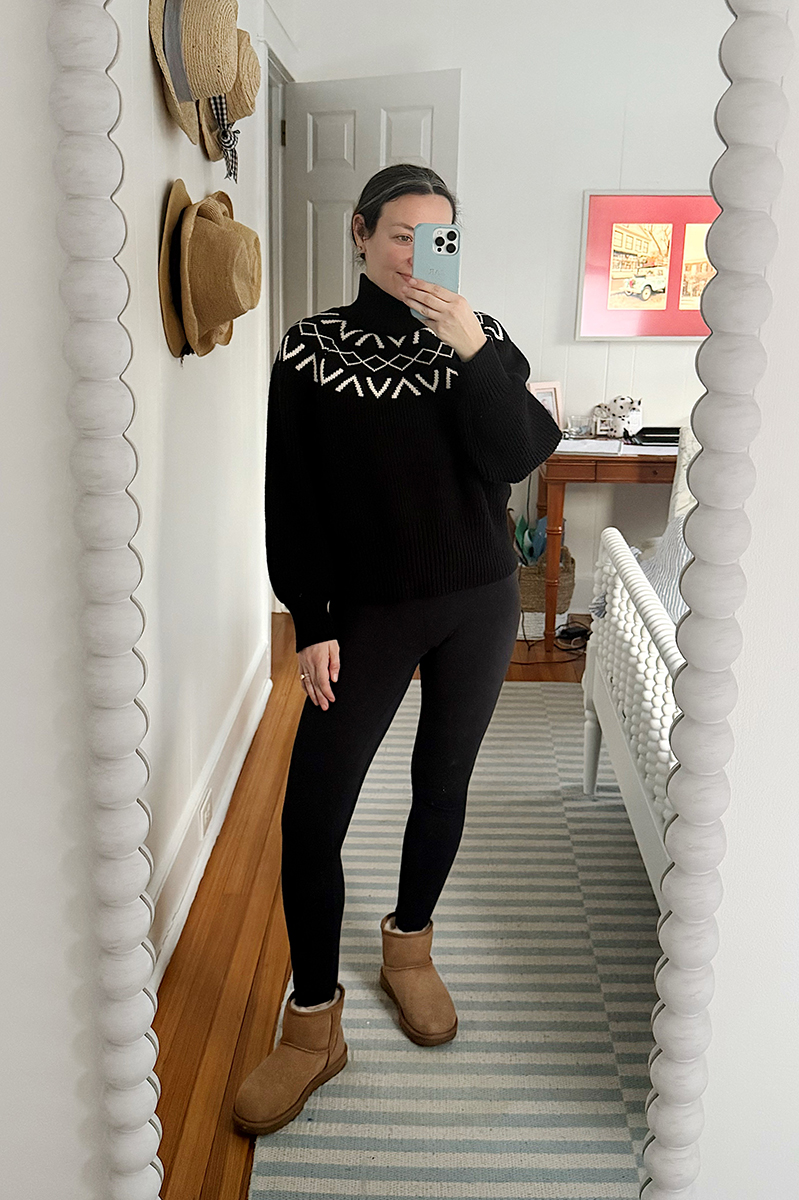 Carly Riordan taking a mirror selfie wearing a black turtleneck, leggings, and ugg boots.